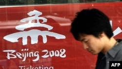 Пекиндегі 2008 жылғы Жазғы олимпиада ойындарына билет жарнамасының жанынан өтіп бара жатқан адам. Пекин, Қытай. 15 сәуір, 2007 жыл.