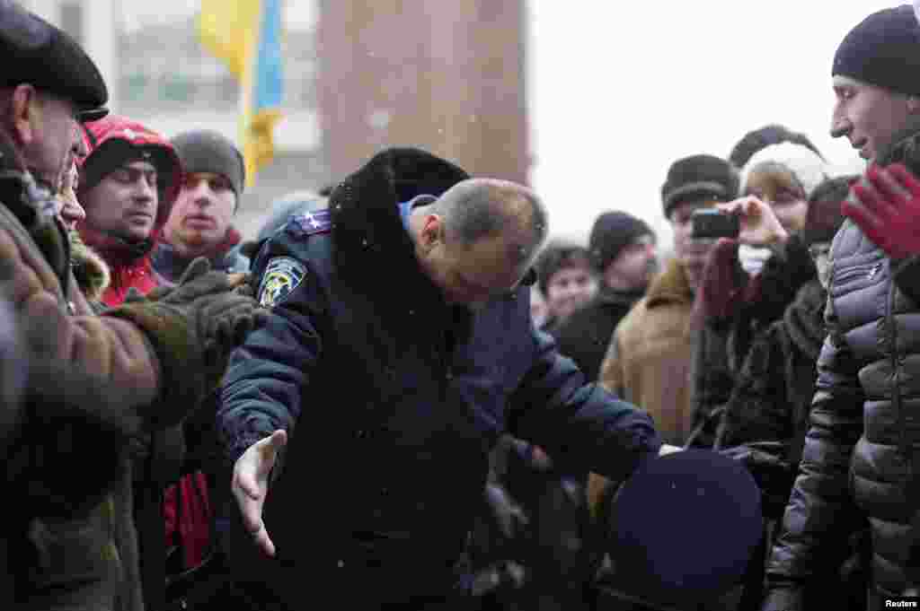 Ukraine - An Interior Ministry member (C) bows his head as he leaves the regional administration headquarters while anti-government protesters attempt to take over during a rally in the town of Ivano-Frankivsk, January 24, 2014. Ukrainian President Viktor