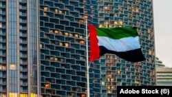 Steagul Emiratelor Arabe Unite fluturând în fața unor zgârie-nori.