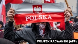 Egy férfi mutatja a lengyel zászlót, miközben lengyel szélsőjobboldali szurkolók vonulnak fel Varsóban az ország függetlenségének napján, 2020. november 11-én