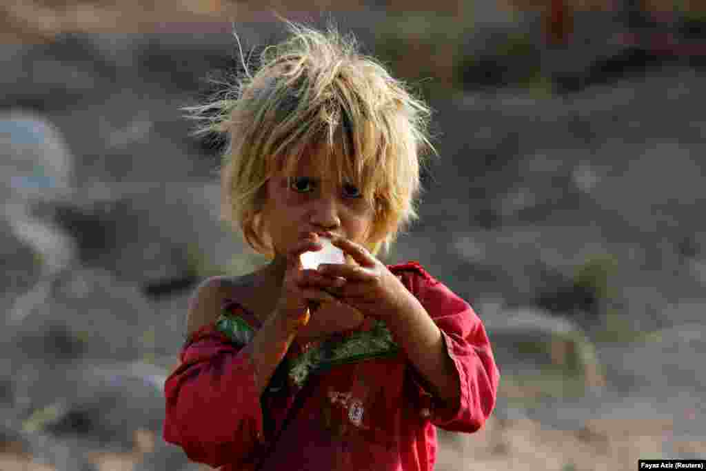 A girl enjoys a piece of ice as she stands outside her family&#39;s tent on the outskirts of Peshawar, Pakistan. (Reuters/Fayaz Aziz)