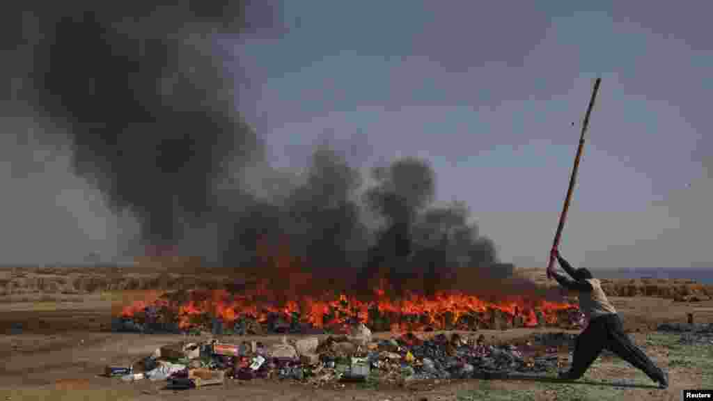 A man from Pakistani customs uses a bamboo stick to destroy bottles of liquor near a burning pile of narcotics on the outskirts of Karachi. (REUTERS/Akhtar Soomro)