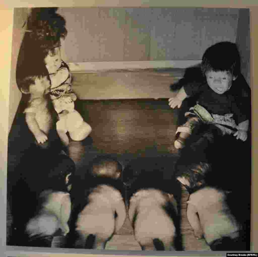 A doll appears to scream in horror at four other dolls lying facedown on the floor.