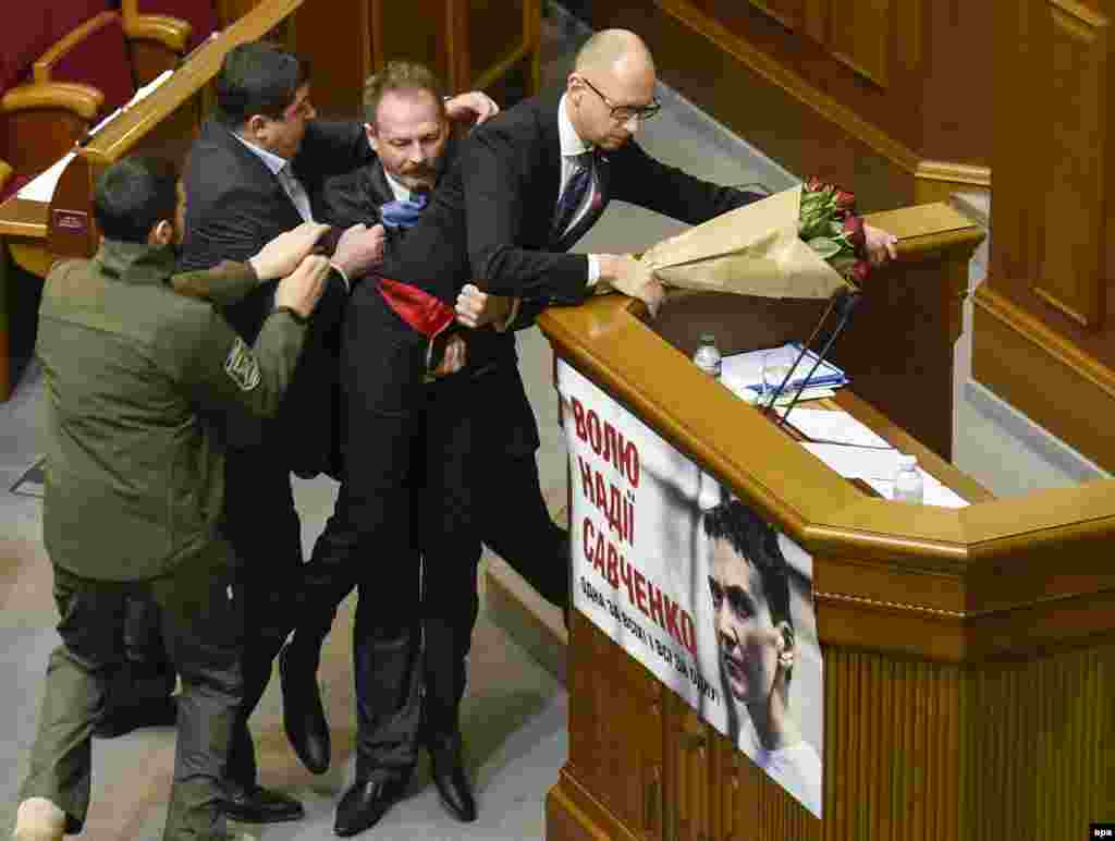 Ukrainian parliament deputy Oleh Barna (2nd right) tries to remove Prime Minister Arseniy Yatsenyuk from the tribune, after presenting him a bouquet of roses, during a parliament session in Kyiv, on December 11. (epa/Aleksandr Kosarev)