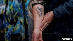 66-летняя Наталья Липей демонстрирует татуировку с позывным своего погибшего сына и эмблемой бригады, в которой он служил, во время посещения импровизированного мемориала павшим украинским защитникам. Киев, площадь Независимости, 17 октября 2025 года