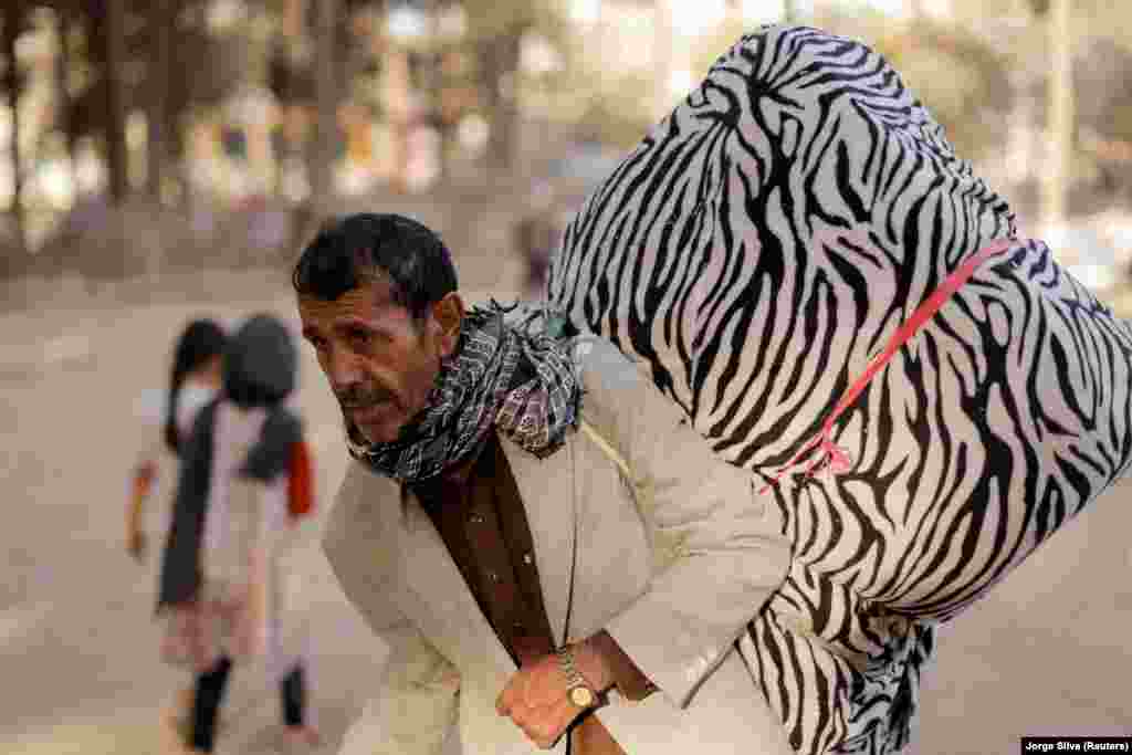 An Afghan man, who is among displaced people fleeing the violence in their provinces, carries his belongings as he prepares to return to his province, at a makeshift shelter at Shahr-e Naw park, in Kabul, Afghanistan October 4, 2021.&nbsp;