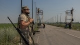Украинский военный стоит на страже, пока его сослуживцы устанавливают антидроновые сетки над дорогой на востоке Донецкой области, 8 июля 2025 года