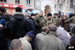 Captured Ukrainian soldiers kneel as the leader of the self-declared Donetsk People's Republic, Aleksandr Zakharchenko (center), stands and members of the media film at a bus stop where 13 people were killed in a trolleybus shelling.