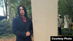 Наталья Садыкова, вдова Айдоса Садыкова, у стелы в Байе 