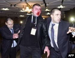 A bloodied Oktay Enimehmedov is led away from the scene of the attack by security personnel.