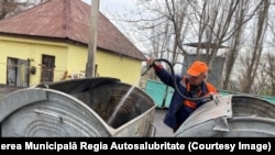 Un angajat al Întreprinderii Municipale „Regia Autosalubritate” din Chișinău curăță un container metalic de gunoi. 