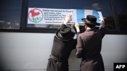 دو عضو گروه لِو طاهور پوستر «کمیته نجات بین‌المللی برای خانواده‌های یهودی عضو لِو طاهور» را به شیشه اتوبوسی در گواتمالاسیتی نصب می‌کنند.