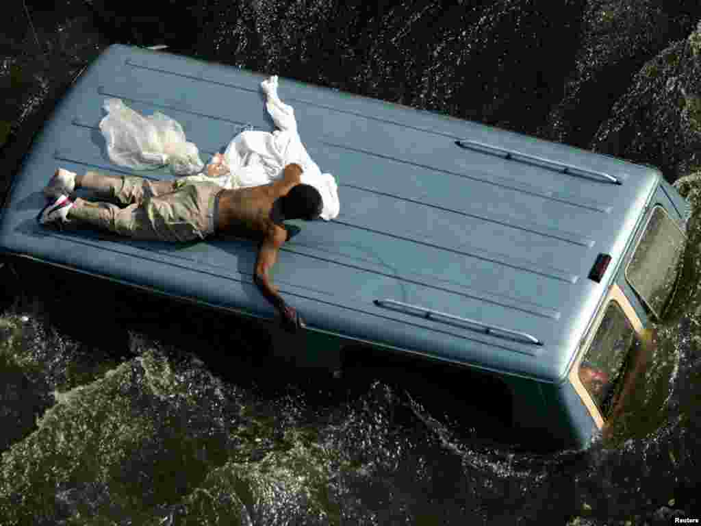 A man clings to the top of a vehicle surrounded by flood water before being rescued by the U.S. Coast Guard in New Orleans.