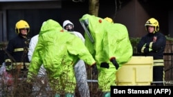 U.K. -- Members of the fire brigade are helped out of their green biohazard suits by colleagues in white protective coveralls after an operation to re-attach the tent over the bench where a man and a woman were found in critical condition sparking a major