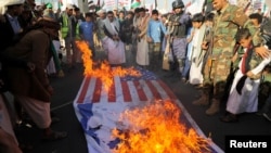 People gather near burning Israeli and U.S. flags as supporters of the Huthi movement rally to denounce air strikes launched by the United States and Britain on Huthi targets, in Sanaa, Yemen, on January 12. 