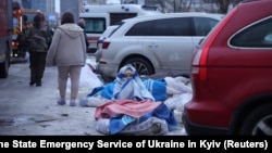 A photo released by the press service of Ukraine's Emergency Service shows a resident sitting on the ground, covered with blankets, at the site of an apartment building hit by a Russian drone in Kyiv, Ukraine, on December 27.