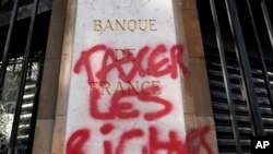 „Taxați bogații” este un slogan care se vede des la protestele sociale din ultima vreme. În imagine: graffiti pe fațada Băncii Naționale a Franței, în aprilie 2023, când francezii au ieșit în stradă să respingă mărirea vârstei de pensionare. (AP Photo/Lewis Joly)