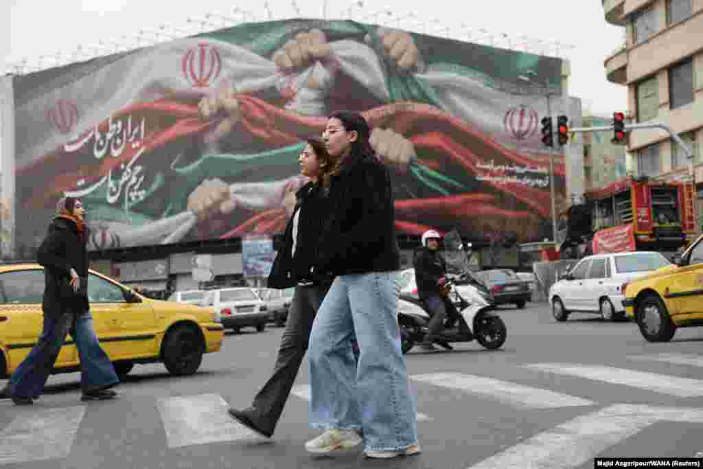 Women walk in Tehran's central Revolution Square. The banner in the background reads: "Iran is our country, its flag our burial shroud."