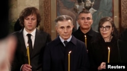 ირაკლი კობახიძე პარტია „ქართული ოცნების“ დამფუძნებელ ბიძინა ივანიშვილთან და მის ცოლთან, ეკატერინა ხვედელიძესთან ერთად სამების საკათედრო ტაძარში ილია მეორის სამოქალაქო პანაშვიდის დროს.