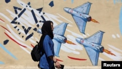 O femeie iraniană trece pe lângă un mural anti-israelian pe o stradă din Teheran. Guvernarea spune că restricționarea comunicațiilor este necesară din cauza agresiunii SUA și Israelului, începută pe 27 februarie.