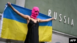 Участница активистской группы Pussy Riot держит украинский флаг во время акции протеста против участия России в Венецианской биеннале перед российским павильоном, 6 мая 2026 года, Венеция