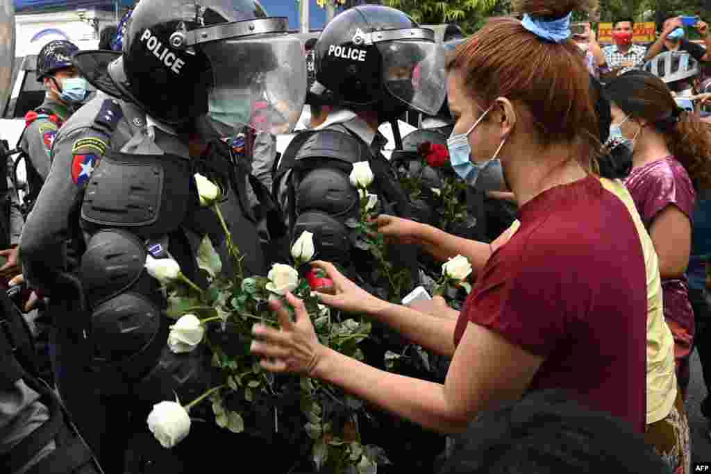 Un protestatar oferă un buchet de flori polițiștilor în timpul unei demonstrații din Yangon (Photo by STR / AFP)