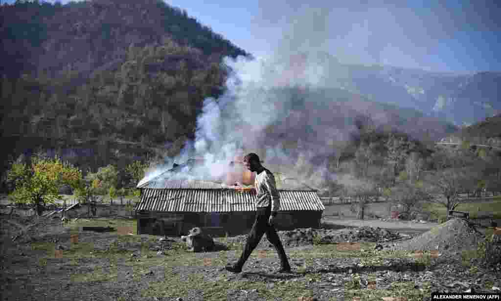 Мужчина проходит мимо горящего дома в селе Чаректар/Чарактар.