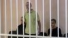 A still image shows Britons Aiden Aslin (left), Shaun Pinner (center), and Moroccan Brahim Saadoun appear in a courtroom cage at a location said to be Donetsk.