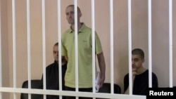 A still image shows Britons Aiden Aslin (left), Shaun Pinner (center), and Moroccan Brahim Saadoun appear in a courtroom cage at a location said to be Donetsk.