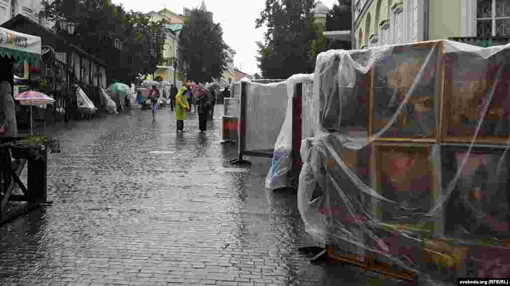 Вэрнісаж пад дажджом. Дождж стаў істотнай перашкодай у гэтым сэнсе: каля гандлёвых шэрагаў практычна няма пакупнікоў, дый самі гандляры не сьпяшаюцца раскладаць тавары, каб яны ня вымаклі
