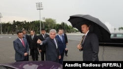 Ziya Mammadov (în centru), prezentându-i președintelui Ilham Aliyev (cu umbrelă) taxiuri londoneze în Baku, în iunie 2011. Ministerul Transporturilor a atribuit contractul de import a 1.000 de taxiuri grupului Baghlan, un holding cu care fiul său, Anar, avea legături financiare.