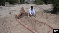 The husband of Farzana Parveen, who was stoned to death by her father and other family members, sits beside her grave. 