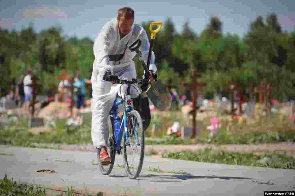 A gravedigger wearing personal protective equipment rides a bike after a funeral of deceased COVID-19 patients on the outskirts of St. Petersburg.