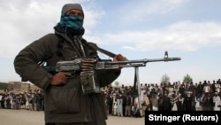 A Taliban fighter and viewers attend the execution of three men in Ghazni Province in 2015.