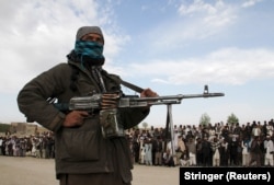 A member of the Taliban and onlookers stand at the site of the execution of three men in Ghazni Province in 2015.