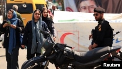 Iranian women walk past a police officer standing guard on on Tajrish Square in Tehran on April 15.