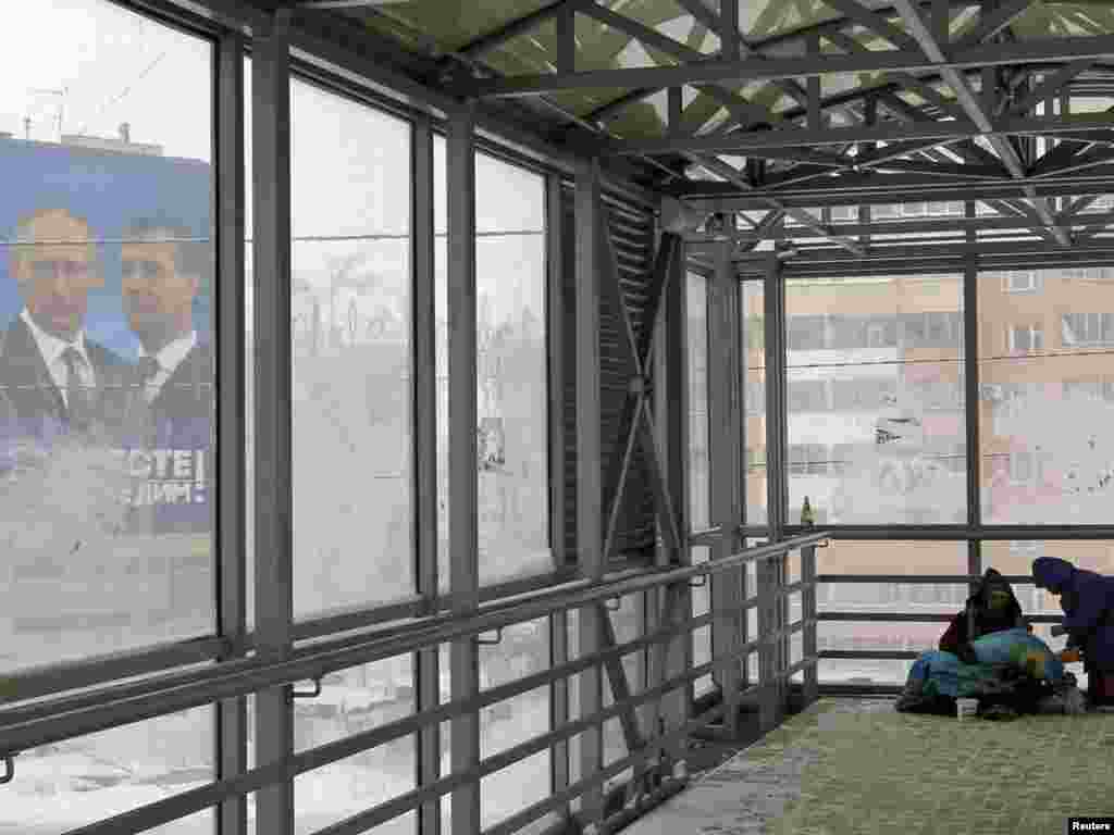 Homeless people shelter in a covered walkway near an election poster for the United Russia party in the city of Kazan, in the Tatarstan Republic, on November 30. (REUTERS/Anton Golubev)