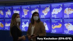 Two women stand near a digital board displaying preliminary results in Russia's regions of the nationwide referendum in July 2020. Critics fear the new system's lack of transparency and voter-verification safeguards could open the way for vote manipulation.