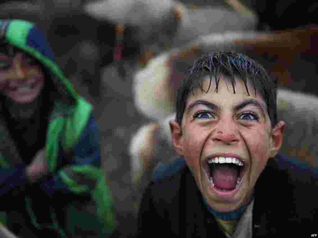 A boy reacts with a laugh as he waits for customers at an animal market on a rainy day on the outskirts of Kabul. - Photo by AFP