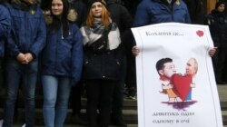 Protestatari cu un afiș arătându-i pe Zelenski și Putin în fața administrației prezidențiale de la Kiev.