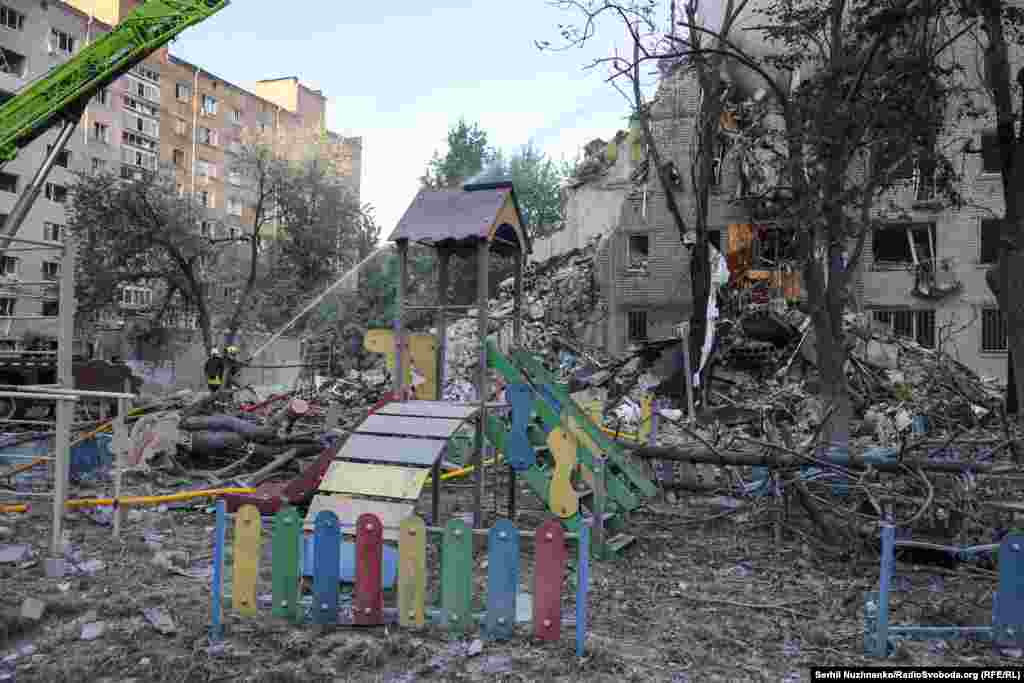 Пошкоджений дитячий майданчик поруч зі зруйнованою багатоповерхівкою