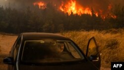 Un localnic intră în mașină la Dione, în Grecia, duminică seară. Autoritățile au ordonat evacuări masive în suburbiile de nord-est ale Atenei, amenințate de incendiile de vegetație. 