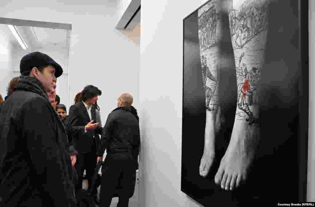 Two men look at a photograph of hanging feet covered with depictions of a battle scene at Shirin Neshat's exhibition.