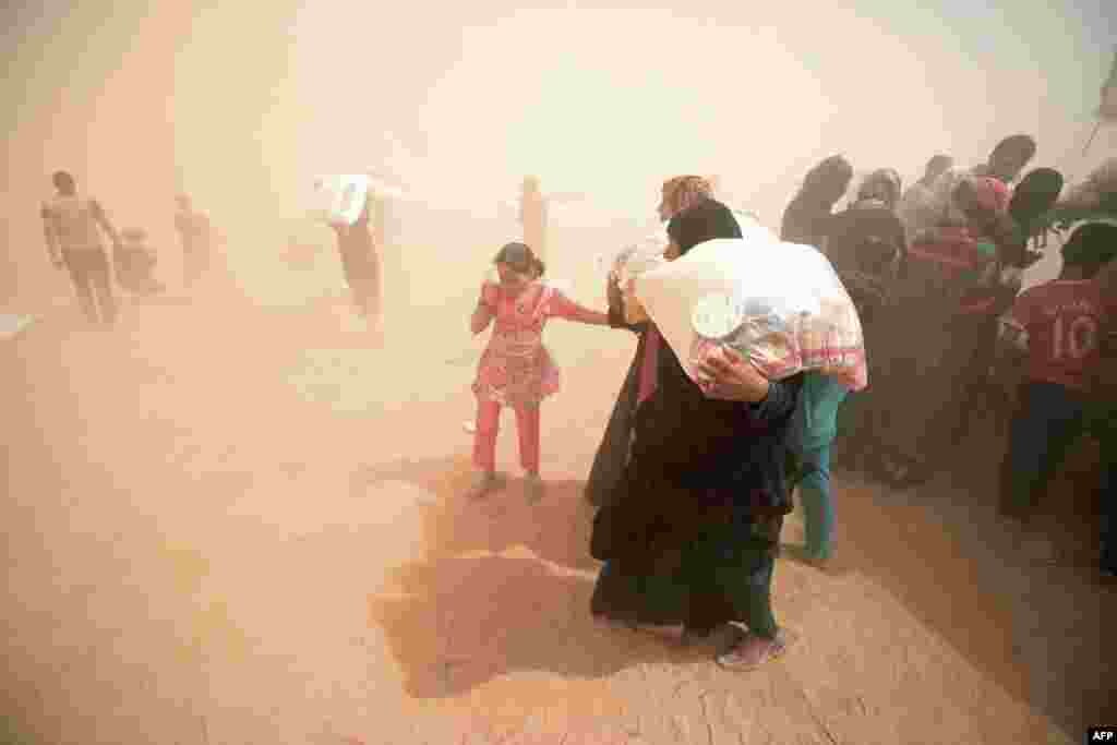 Displaced Iraqis who fled the government&#39;s operation against the Islamic State (IS) group in the city of Fallujah carry basic food items donated by an NGO called Preemptive Love Coalition amid a dust storm. (AFP/Haidar Muhammad Ali)