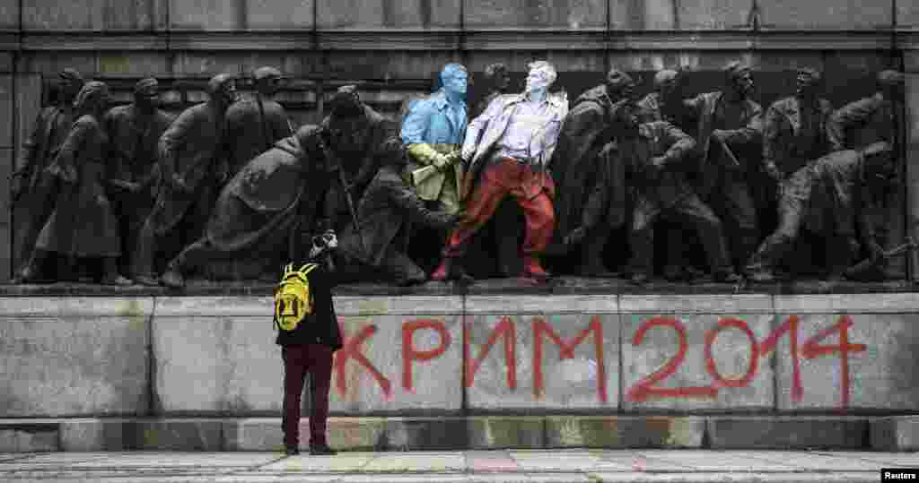 A man takes pictures of figures of a Bulgarian communist-era monument painted in the colors of the Ukranian and Polish flags by unknown people in Sofia. (Reuters/Stoyan Nenov)