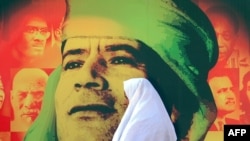 A woman walks past a picture of Libyan leader Muammar Qaddafi in Tripoli.