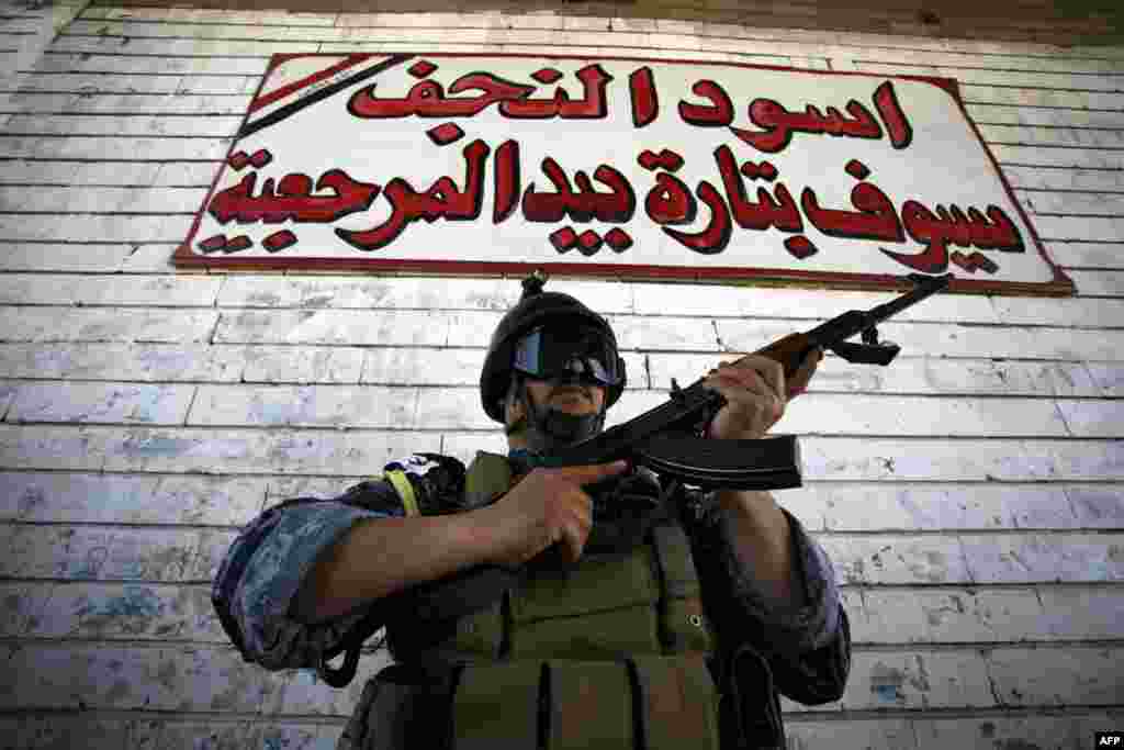 An Iraqi Shi'ite fighter from the Popular Mobilization units, part of the Zahraa Brigade, poses for a picture under a sign that reads in Arabic, "Lions of Najaf," during a training exercise in the central Iraqi city of Kufa. (AFP/Haidar Hamdani)