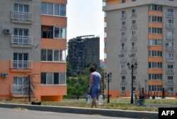 A woman carries bottles with water in the Russian-controlled Azov Sea port city of Mariupol in southeastern Ukraine on July 14, 2025, amid the ongoing Russian-Ukrainian conflict.