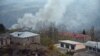 NAGORNO-KARABAKH -- A truck loaded with firewood and other items is seen on a road in the town of Lachin (Berdzor) as smoke rises from a burning house set on fire by departing residents, November 30, 2020