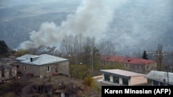 NAGORNO-KARABAKH -- A truck loaded with firewood and other items is seen on a road in the town of Lachin (Berdzor) as smoke rises from a burning house set on fire by departing residents, November 30, 2020